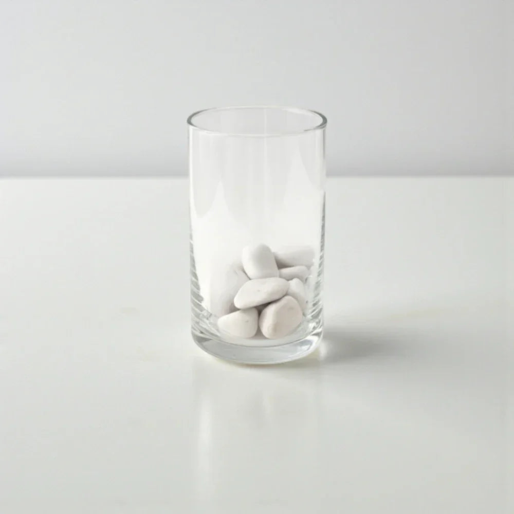 כוס זכוכית שקופה עם אבנים לבנות על שולחן לבן, עיצוב מינימליסטי