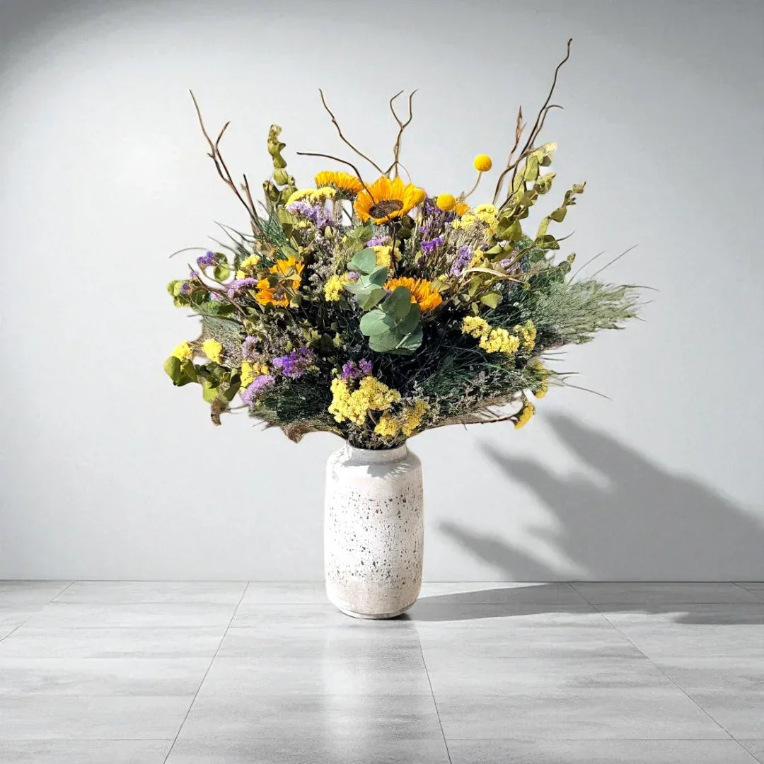 זר פרחים צבעוני בוורכה לבנה על רצפת אריחים אפורה ורקע קיר לבן