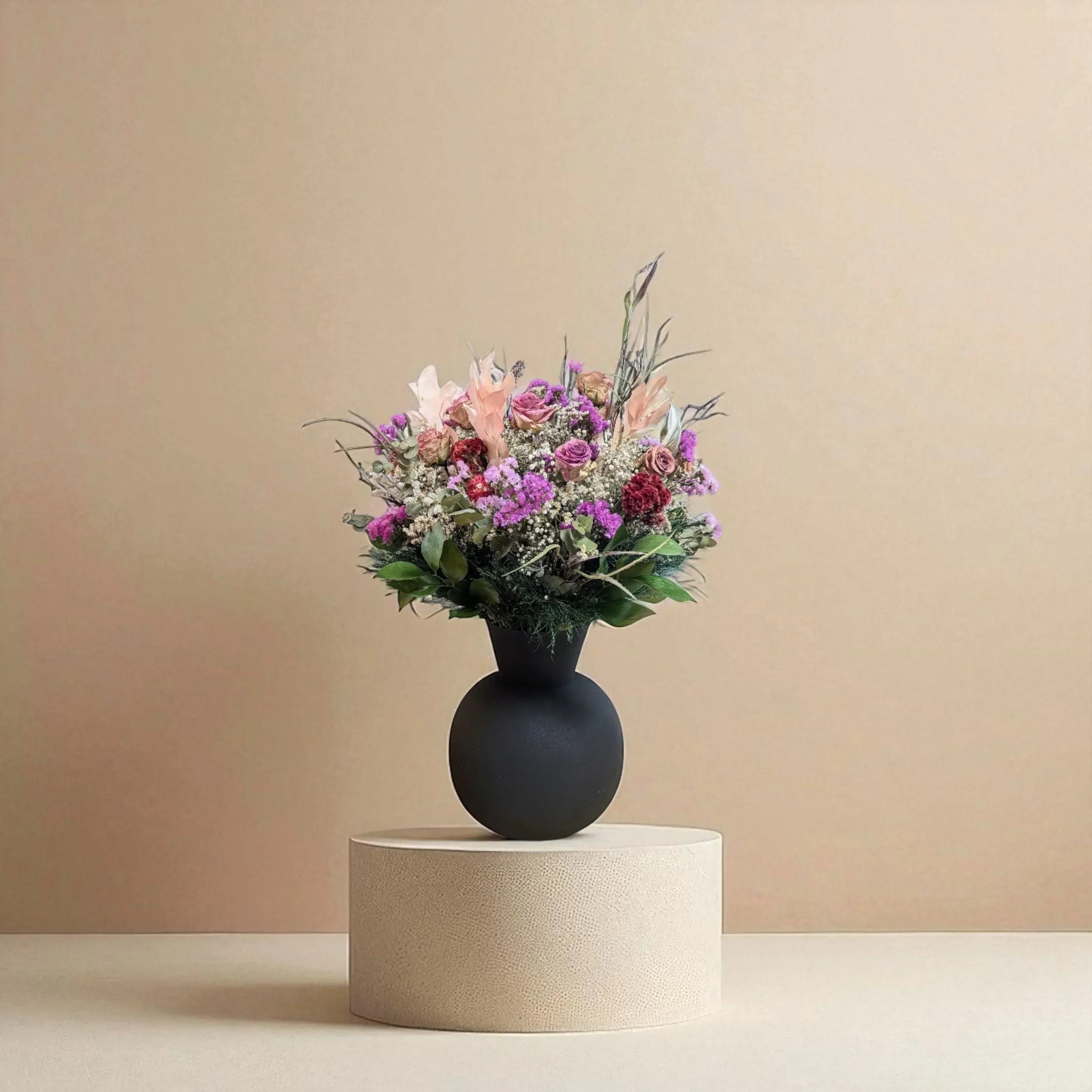 אגרטל שחור עגול עם זר פרחים צבעוניים ורנדומליים על פודיום לבן עגול רקע נייטרלי