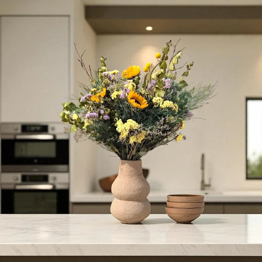 זר פרחים יבש בצבעים צהובים וכתומים בו vase חרס על שיש במטבח מודרני עם קערות חרס חומות