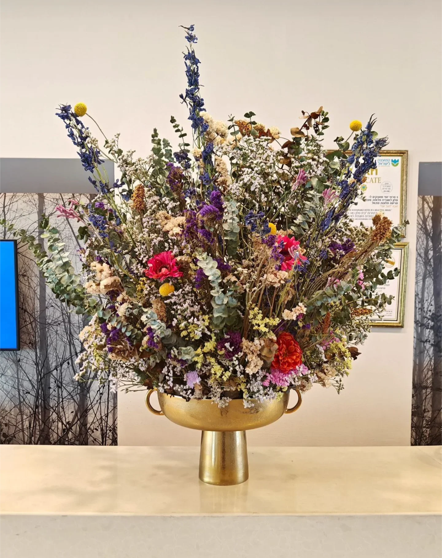 סידור פרחים צבעוני בכלי זהב מרהיב על שולחן עם רקע קיר ופרסומים