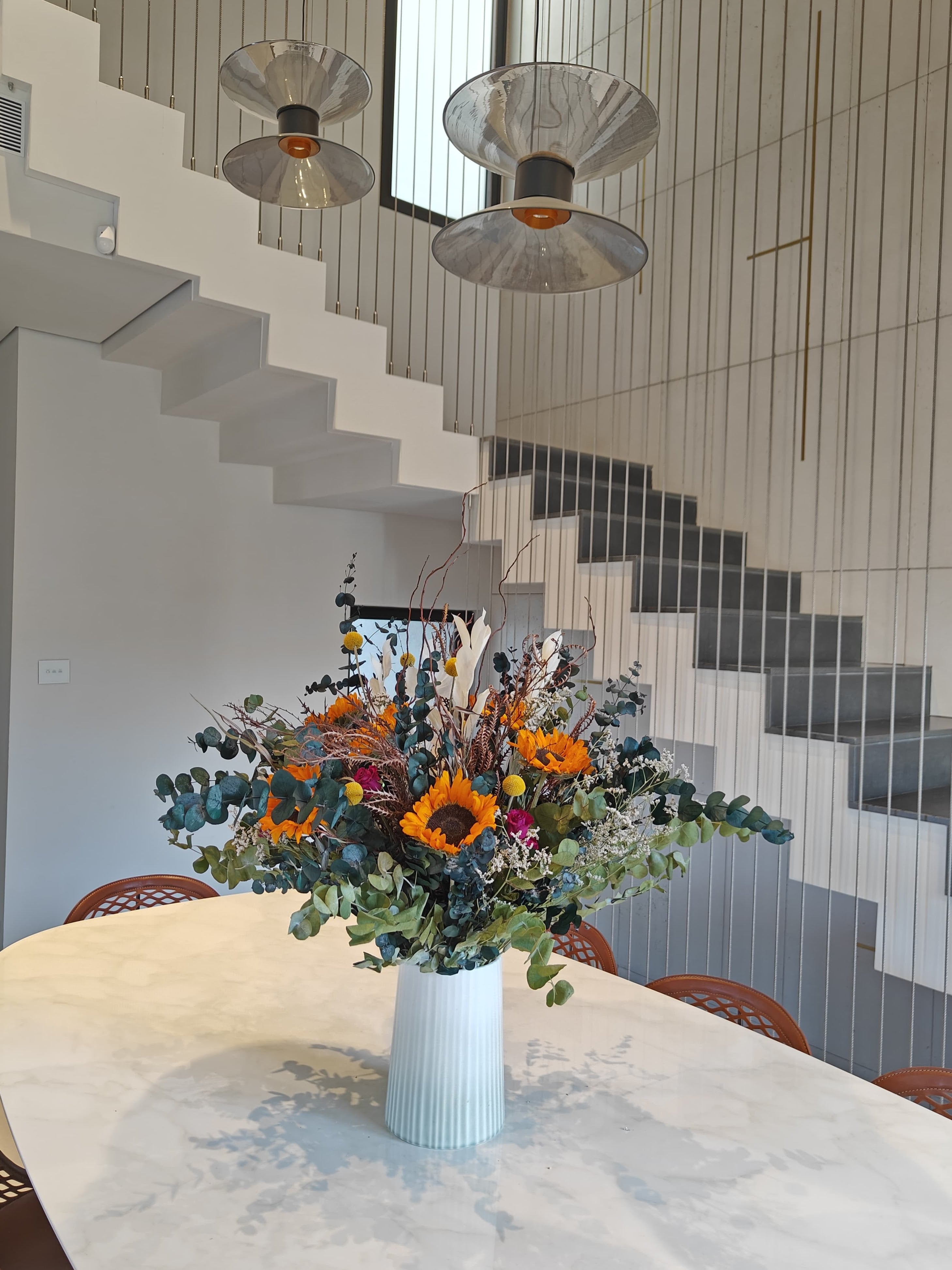 Floral arrangement in a vase on a table with a modern staircase in the background